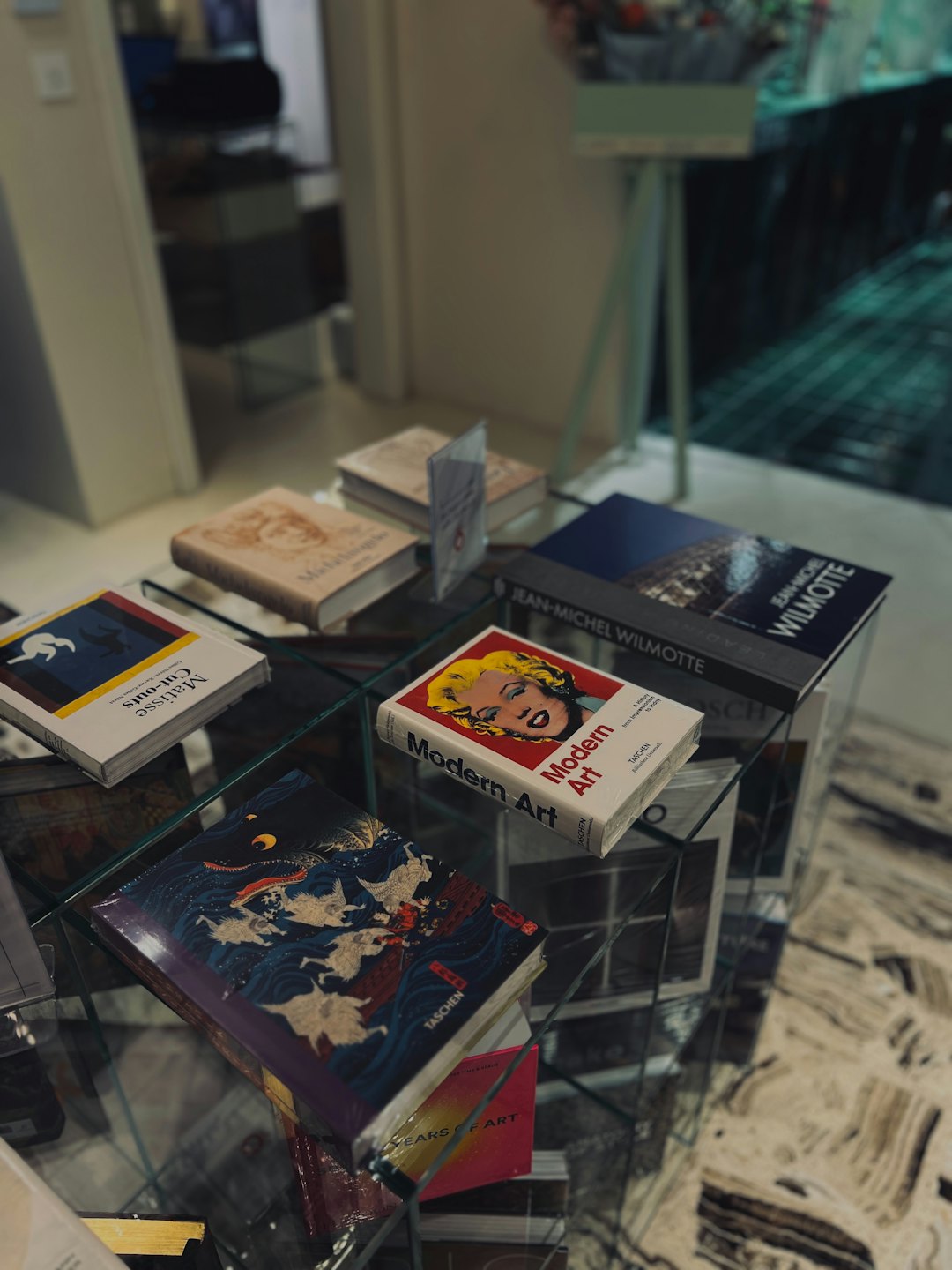 كتب فنية مكدسة ومفتوحة على طاولة زجاجية.